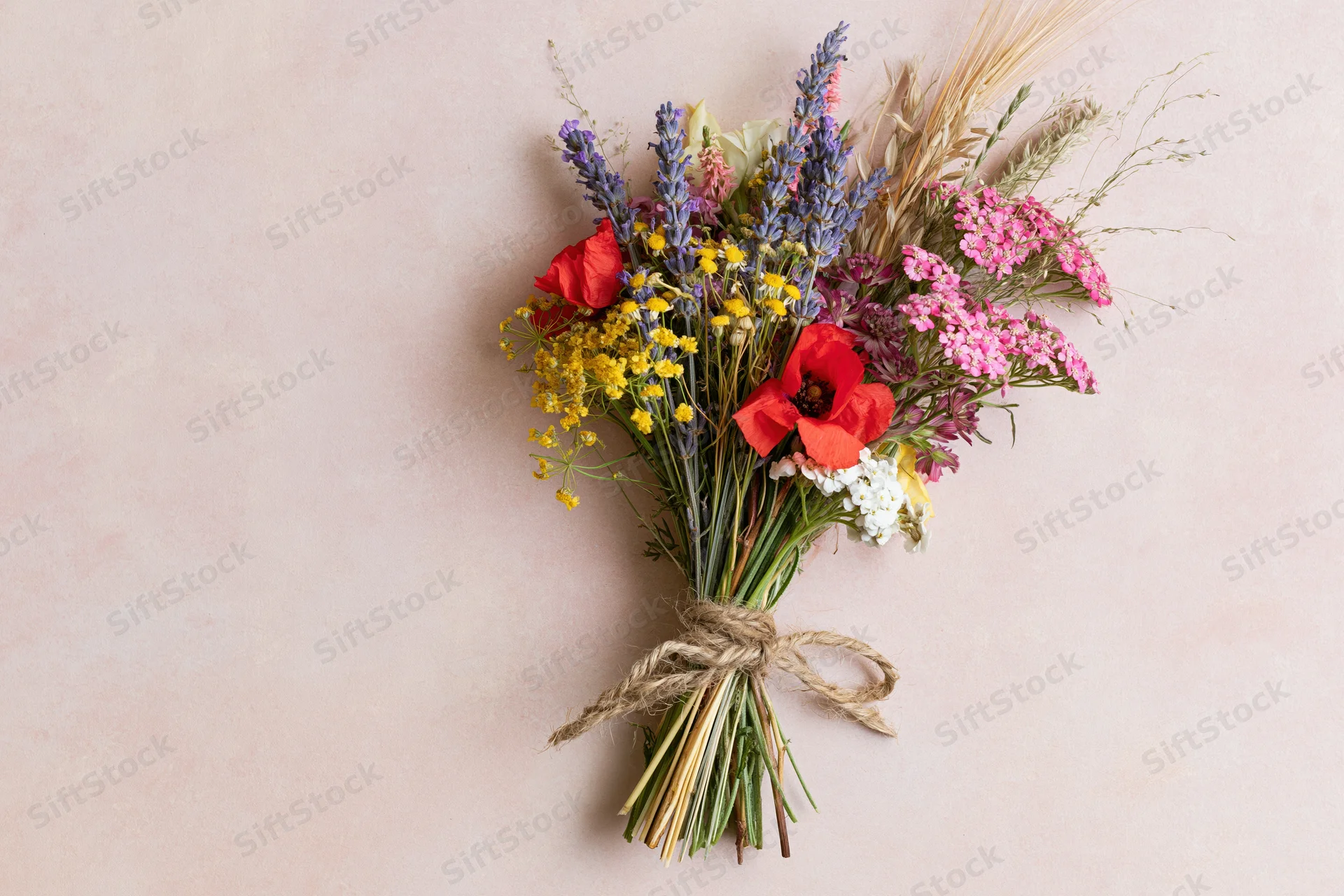 Loose wildflower bouquet tied with twine lying flat on pale blush pink surface