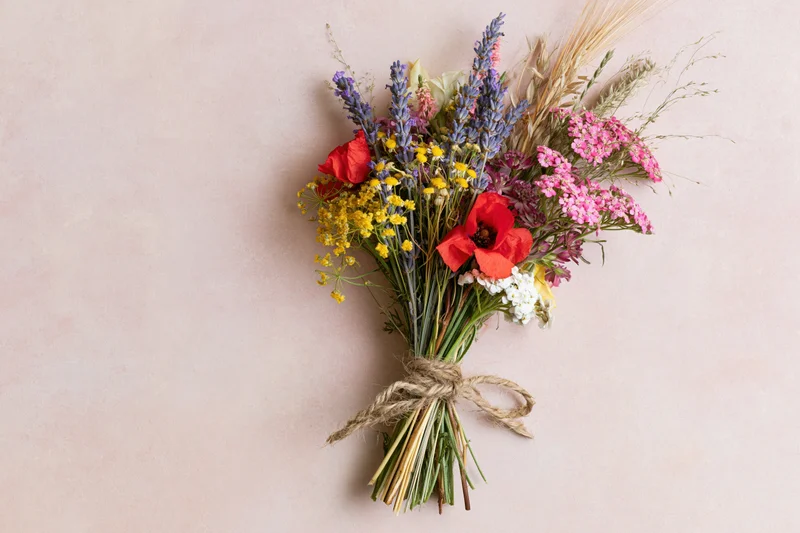 Loose wildflower bouquet tied with twine lying flat on pale blush pink surface