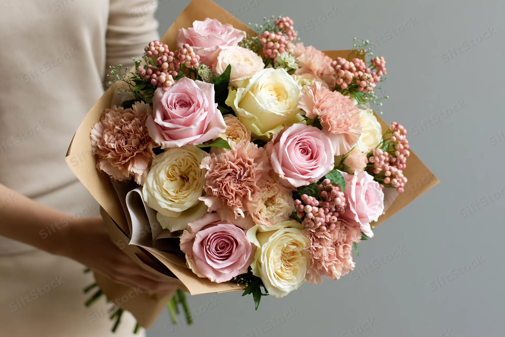 Woman holding a mixed bouquet of soft pink and cream roses wrapped in brown paper