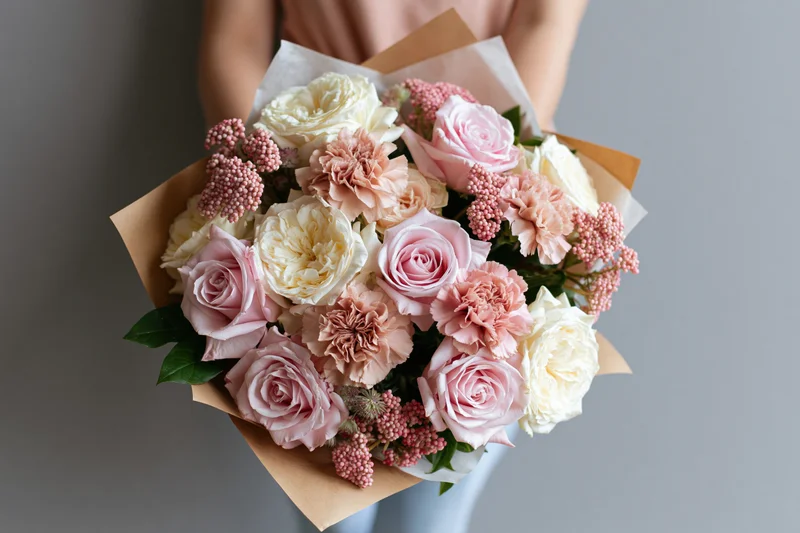 Woman holding a mixed bouquet of soft pink and cream roses wrapped in kraft paper