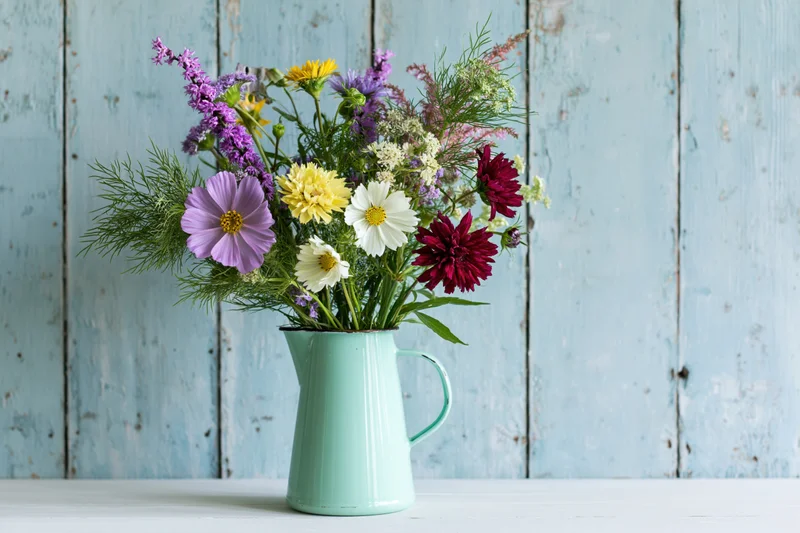 Mixed wildflowers in a mint enamel pitcher on a white table against blue wooden background