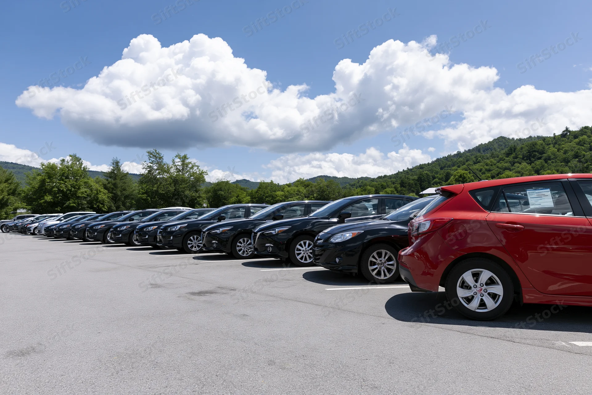 Row of cars parked in an outdoor lot under a blue sky with clouds