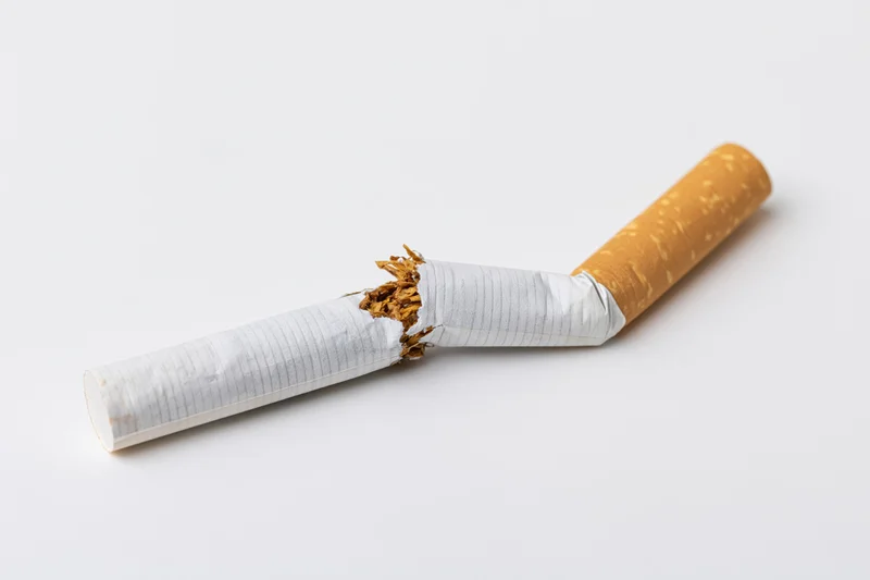 Broken cigarette lying on white surface with torn tobacco exposed