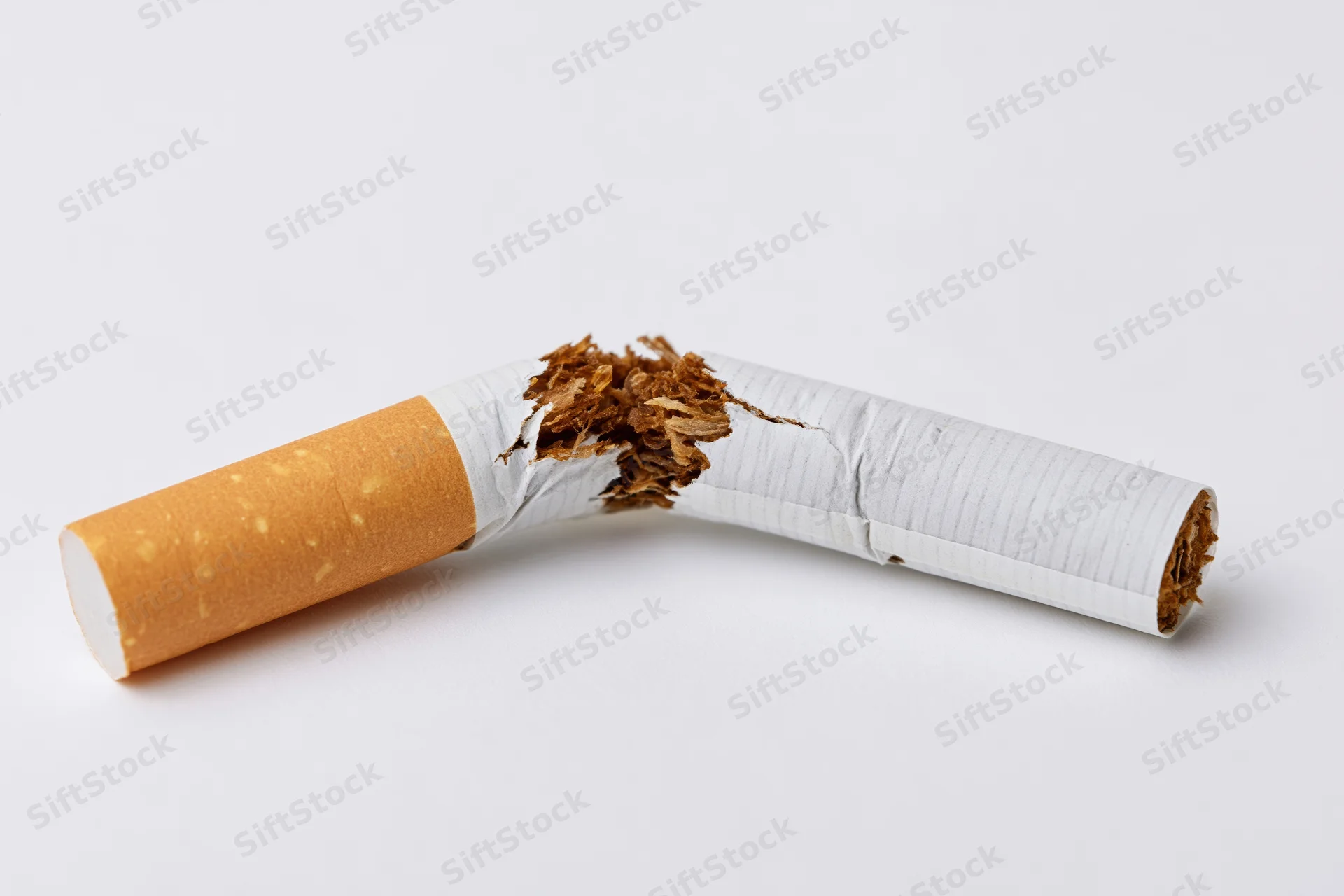 Broken cigarette snapped in half lying on white surface