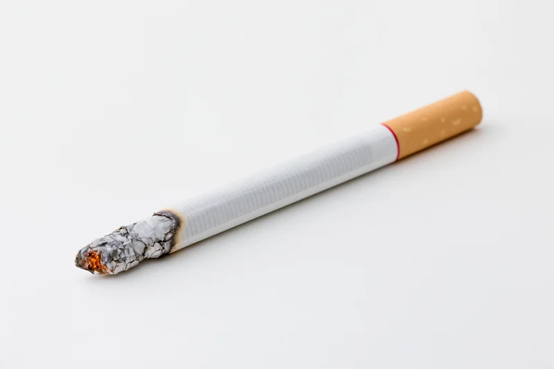 Lit cigarette with glowing ash tip on white background