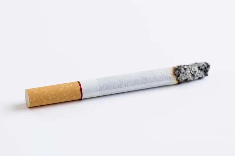 Lit cigarette with ash tip on white background