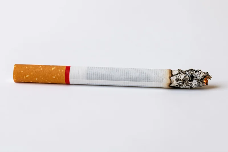 Lit cigarette with glowing ash tip on white background