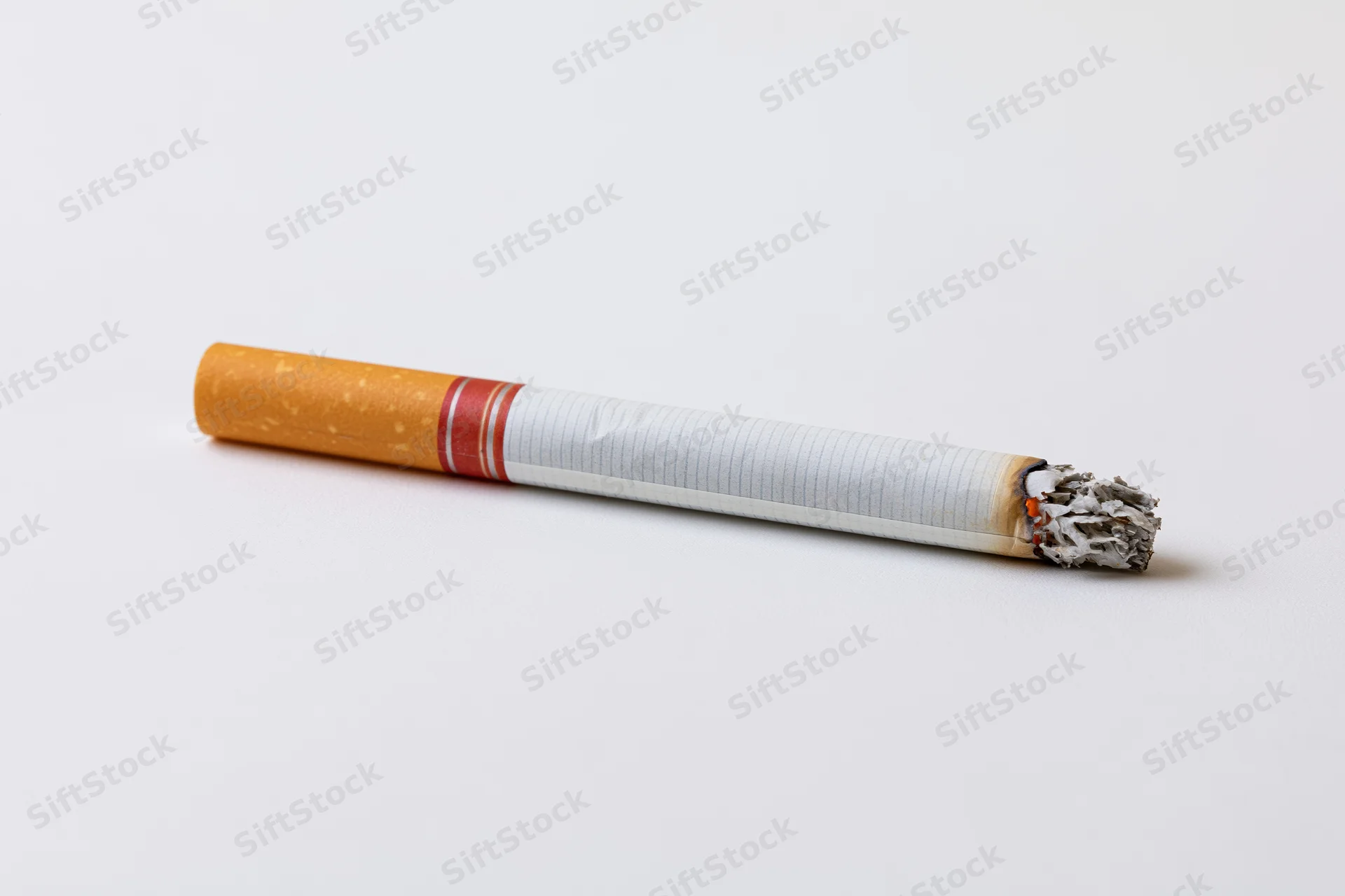 Lit cigarette with ash resting on white surface