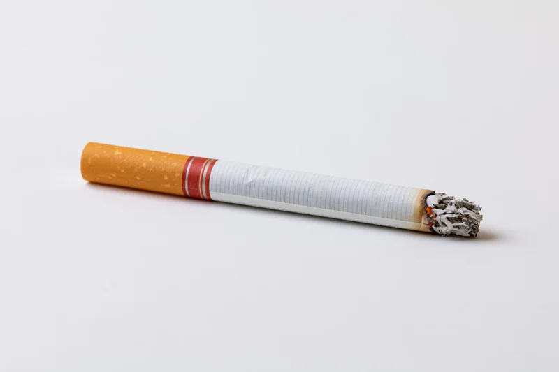 Lit cigarette with ash resting on white surface