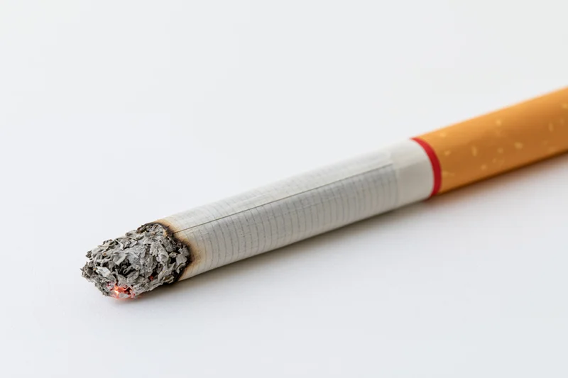 Lit cigarette with glowing ash tip on white surface