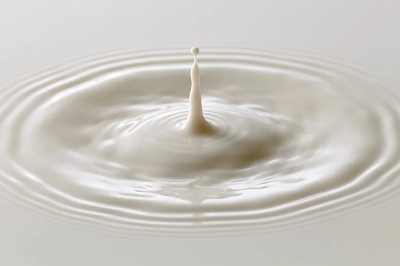 Milk drop frozen mid-splash creating ripples on a smooth surface