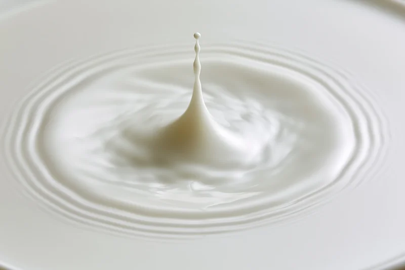 Milk drop frozen mid-splash creating ripples on a white surface