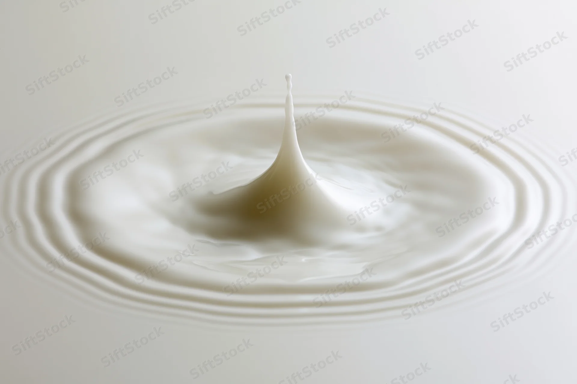 Milk drop frozen mid-splash creating ripples on a smooth white surface