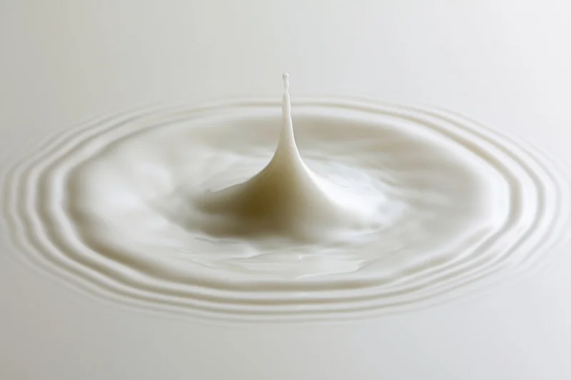 Milk drop frozen mid-splash creating ripples on a smooth white surface
