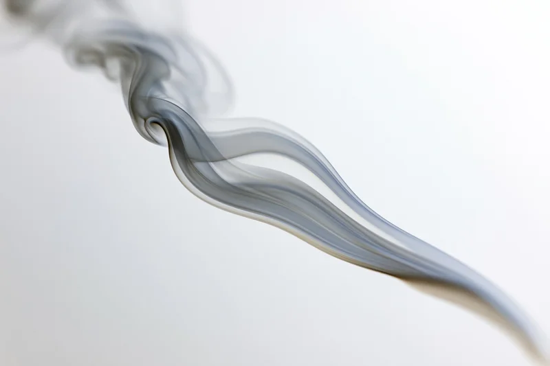 A thin wisp of smoke curling upward against a soft white background
