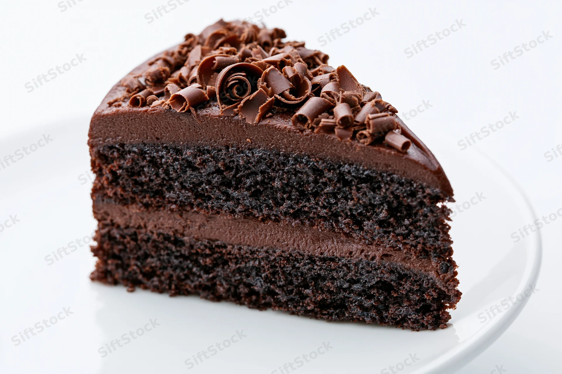 Triangular slice of triple-layer chocolate cake with chocolate curls on white plate
