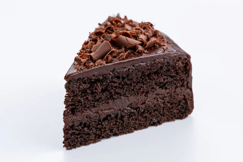 Triangular slice of triple-layer chocolate cake with chocolate curls on white background