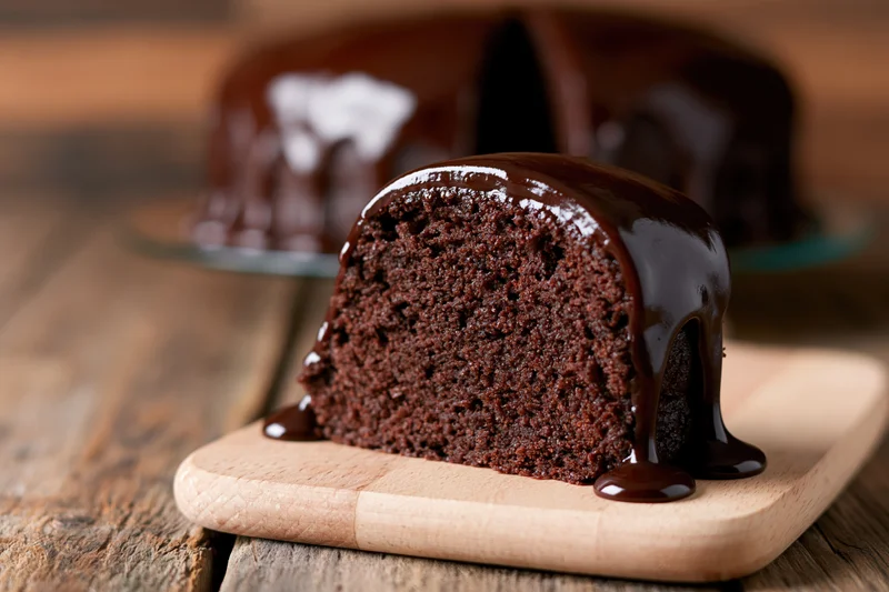Slice of dark chocolate cake with ganache dripping onto board