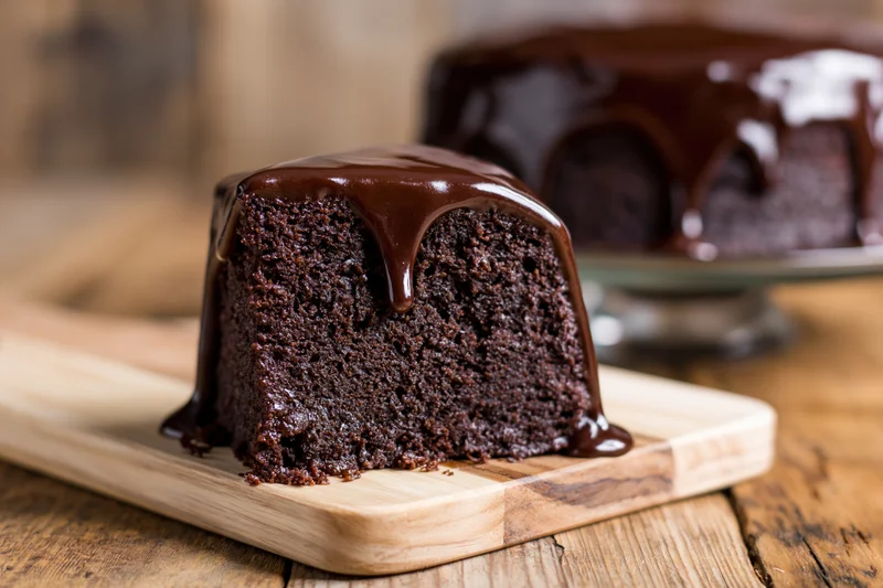 Slice of dark chocolate cake with ganache on board