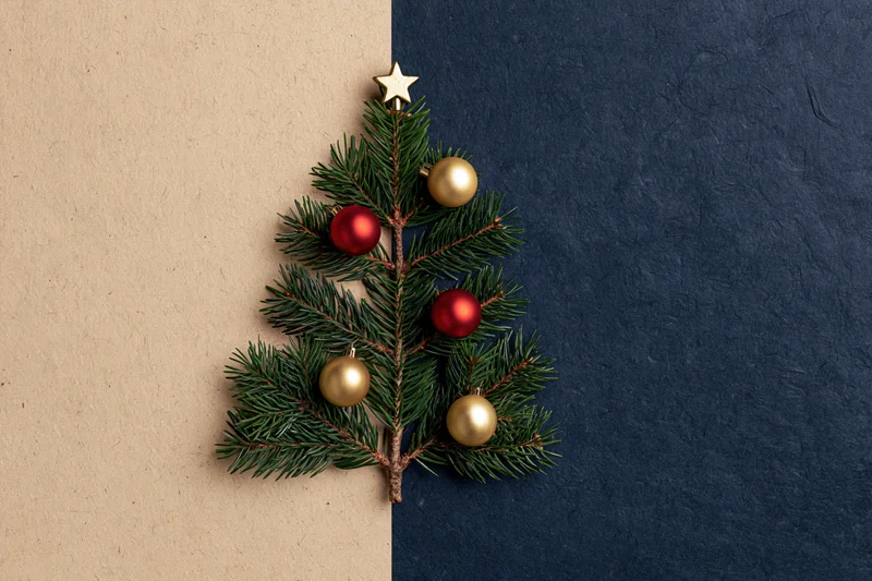 Small christmas tree made from pine branches decorated with red and gold baubles and a star on split beige and navy background