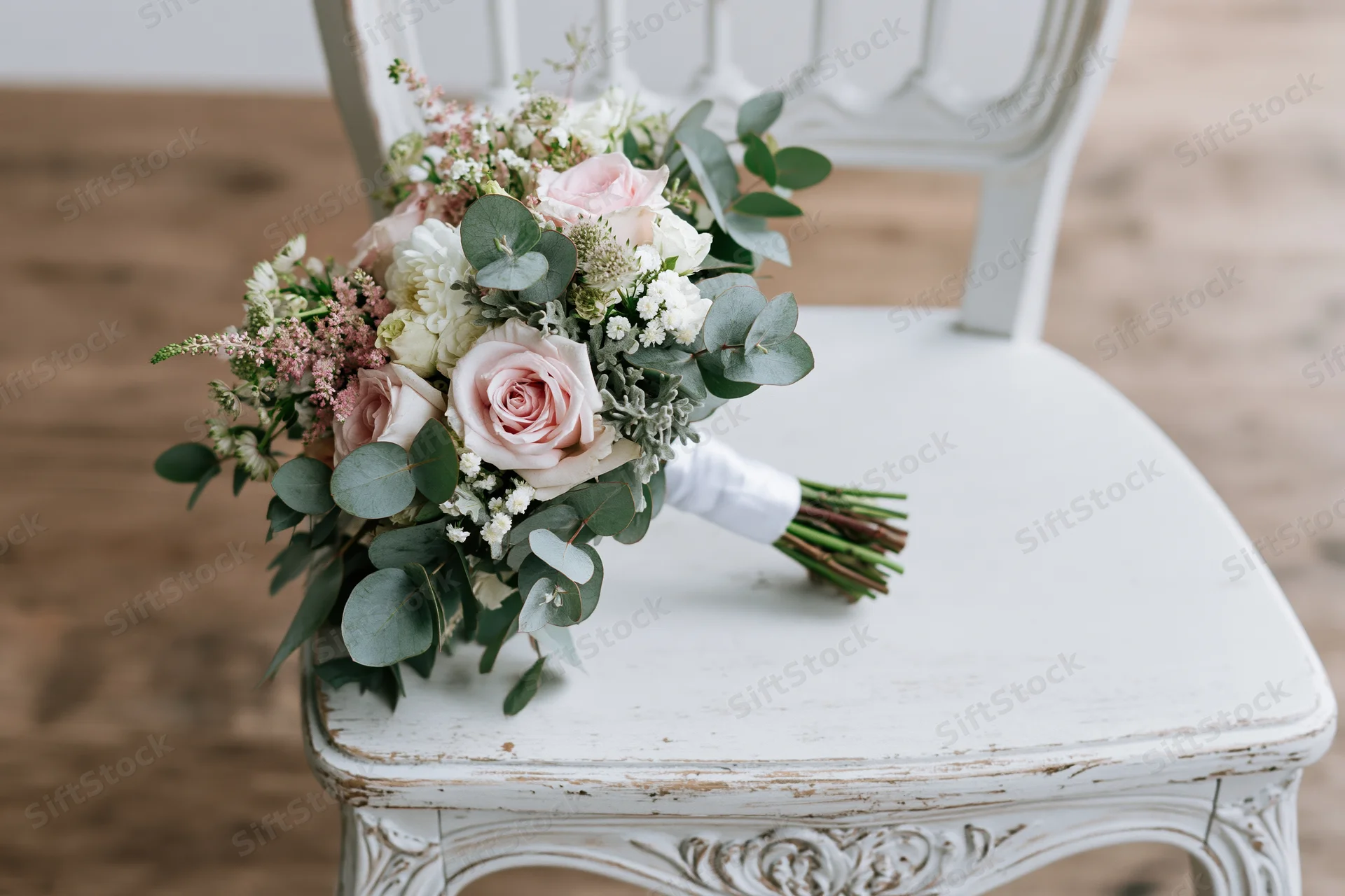 Bridal bouquet with pink roses and greenery resting on a white distressed chair