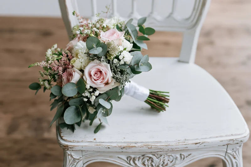 Bridal bouquet with pink roses and greenery resting on a white distressed chair