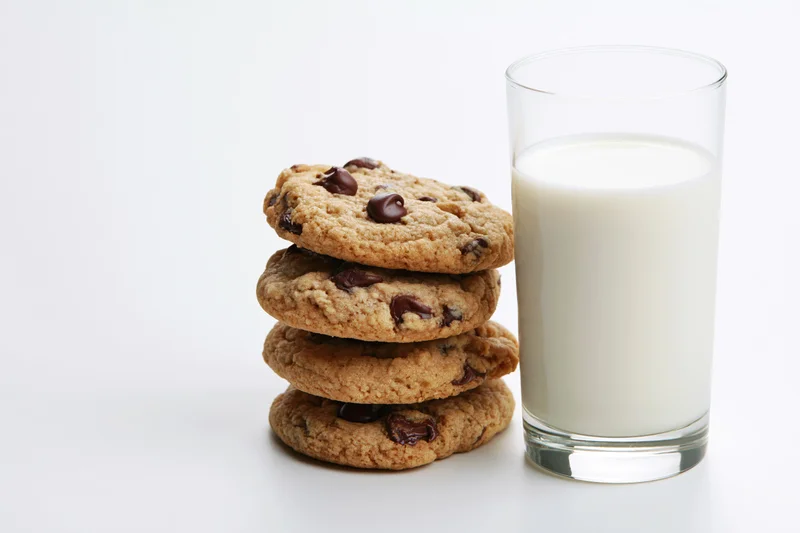 Stack of chocolate chip cookies beside a full glass of milk on white background