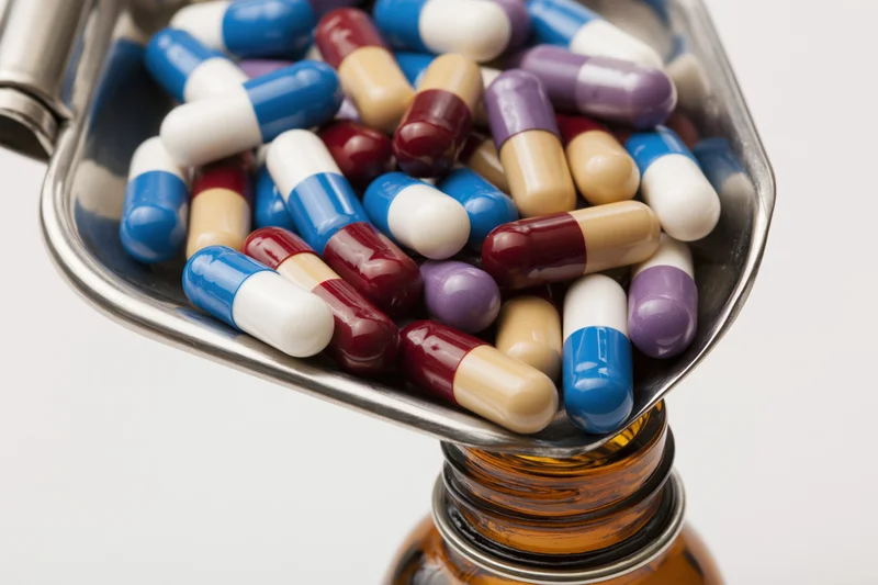 Stainless steel tray holding colorful capsules above an amber medicine bottle