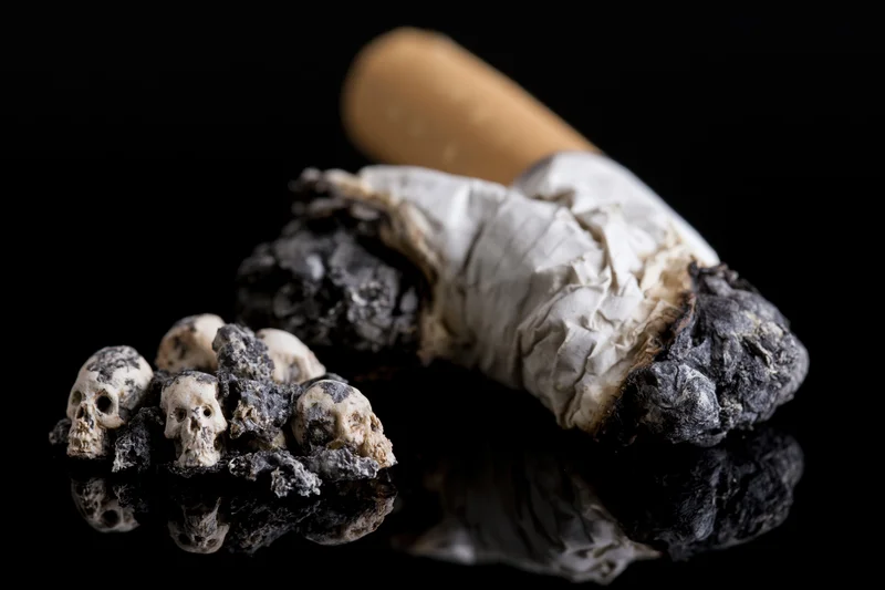 Crushed cigarette butt with ash and tiny skulls on reflective black surface