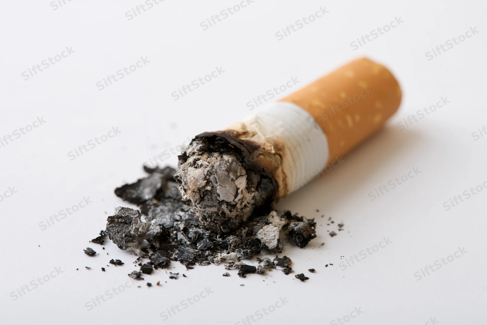 Stubbed-out cigarette butt with ash scattered on a plain white surface