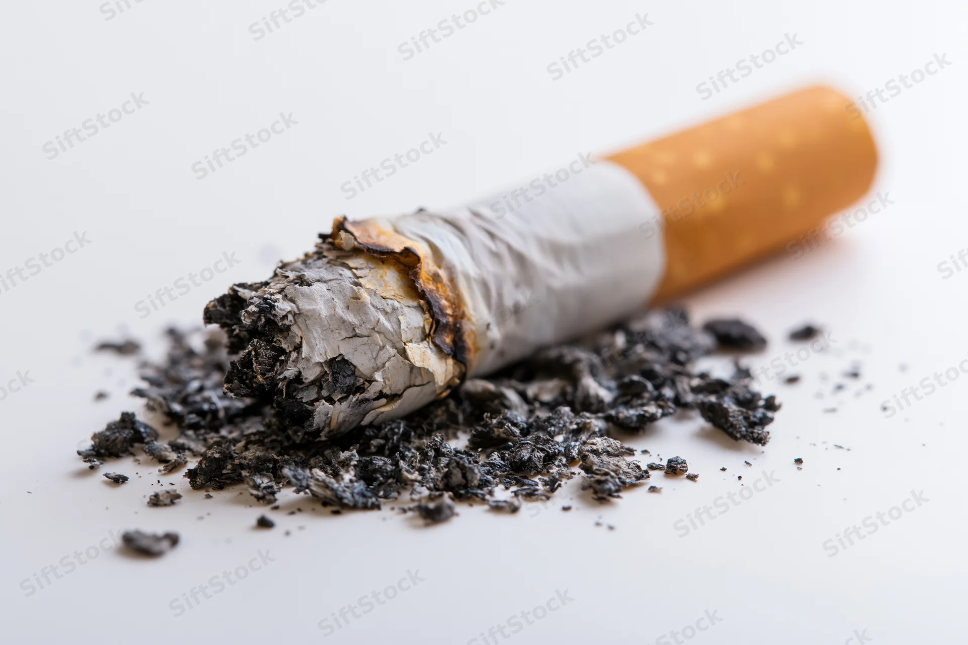 Stubbed-out cigarette butt with ash scattered on a plain white surface