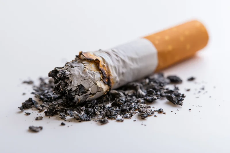 Stubbed-out cigarette butt with ash scattered on a plain white surface