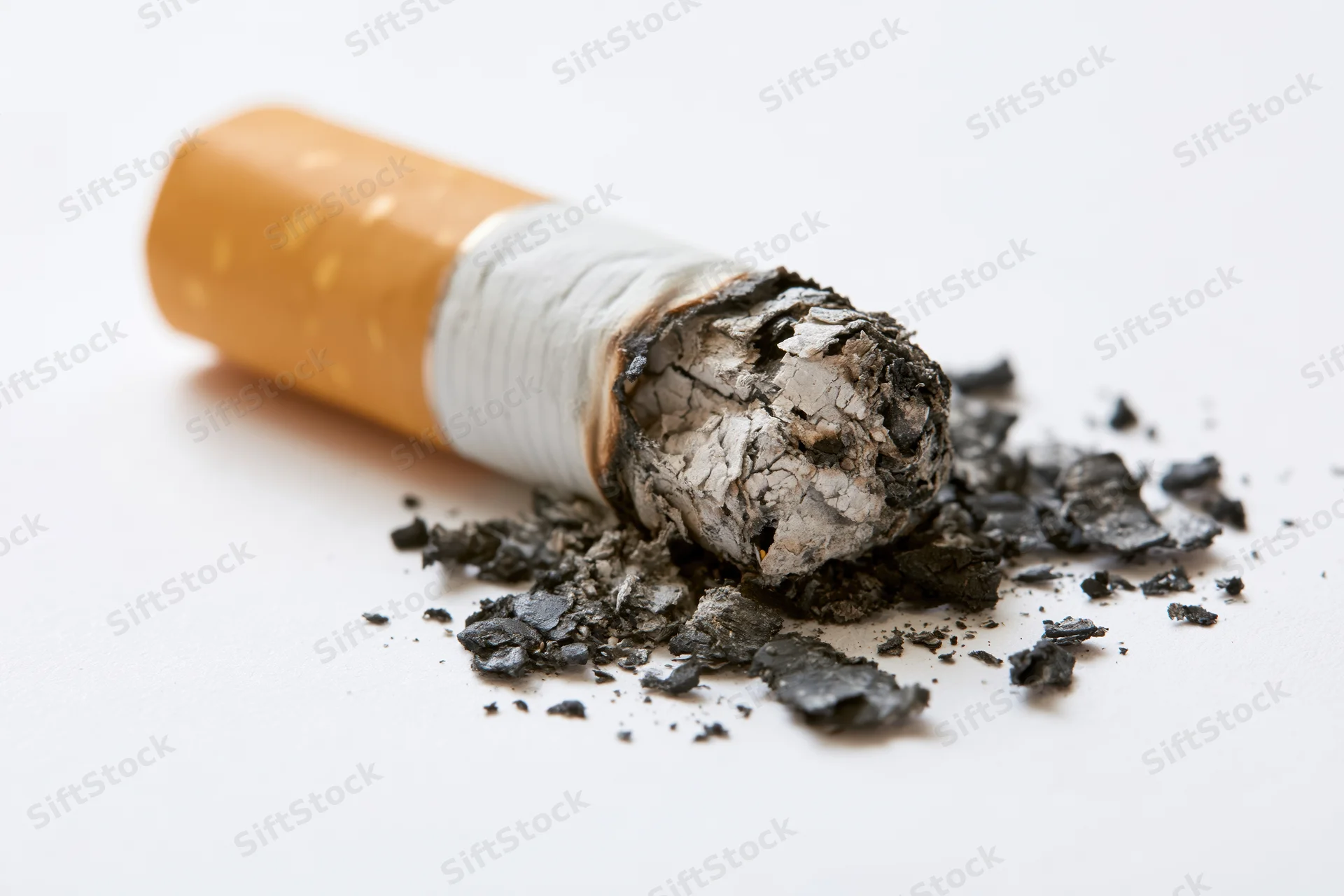 Stubbed-out cigarette butt with ash and debris on white surface