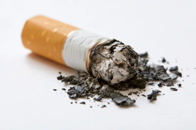 Stubbed-out cigarette butt with ash and debris on white surface