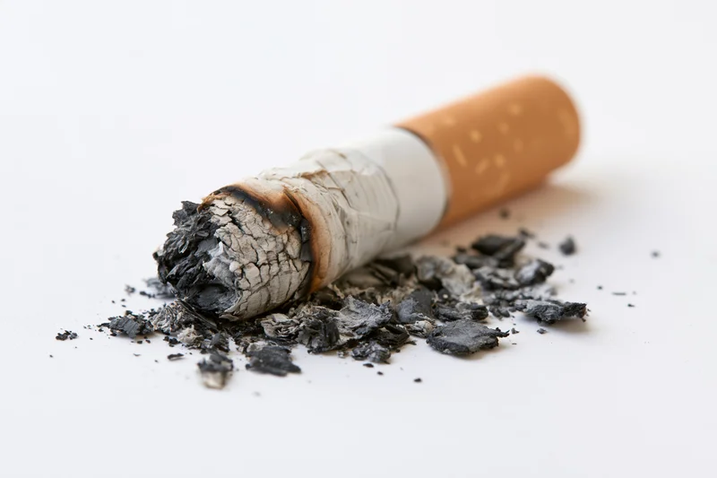 Stubbed-out cigarette butt with ash and debris on white surface