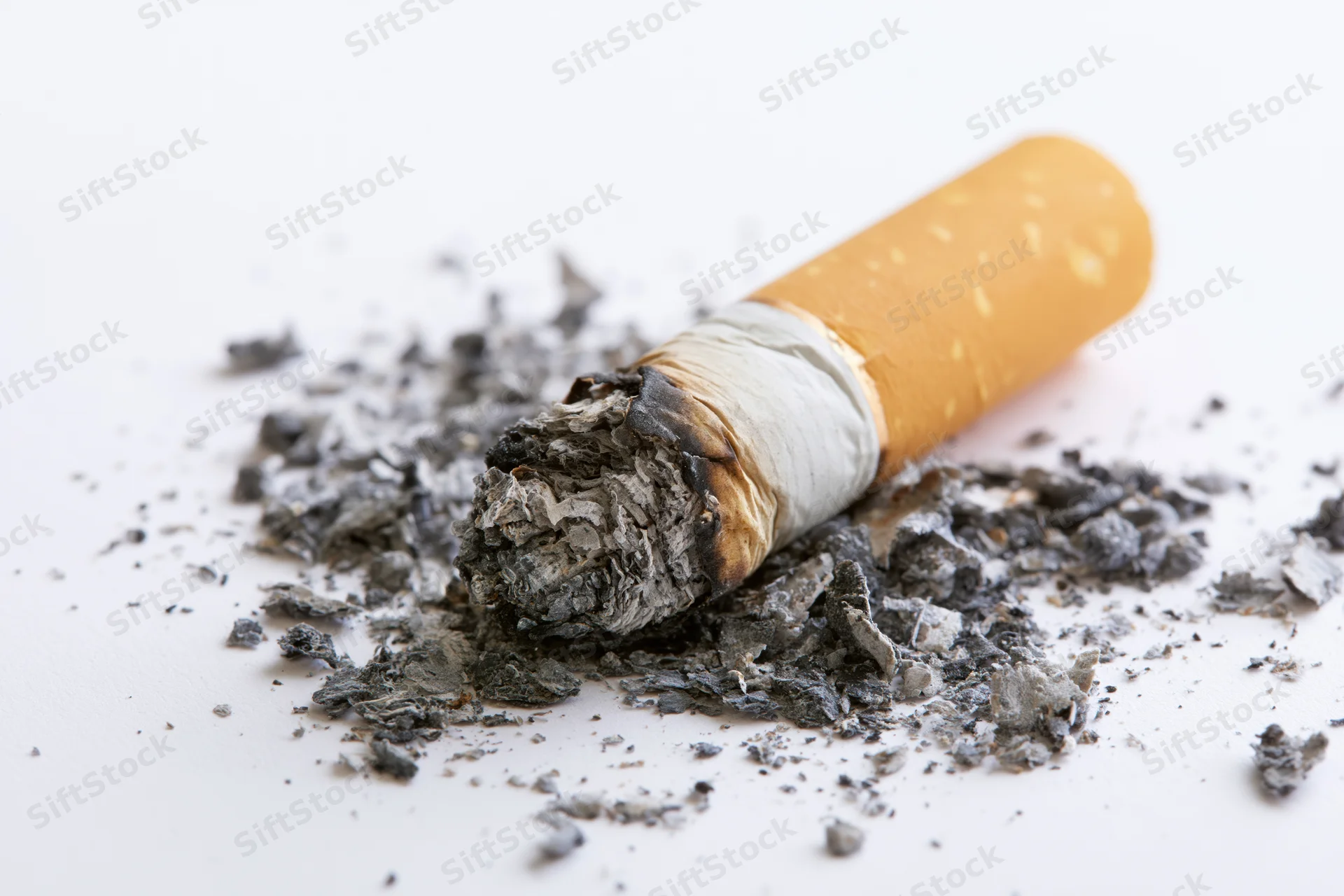 Stubbed-out cigarette butt with ash scattered on white surface