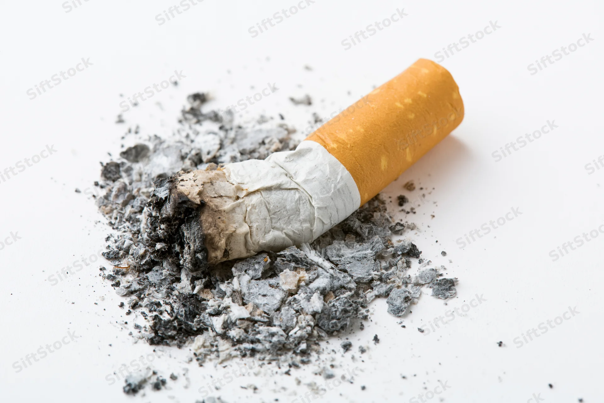 Stubbed-out cigarette butt surrounded by ash on a white surface