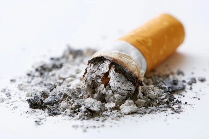 Crushed cigarette butt with ash scattered on white surface