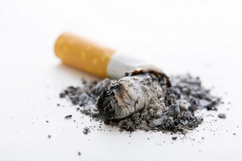 Stubbed-out cigarette butt with ash pile on white surface