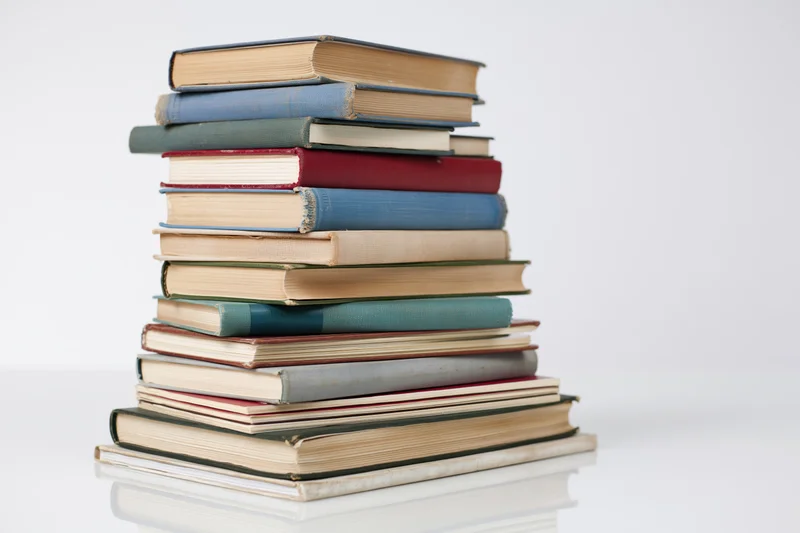 Tall stack of vintage hardcover books arranged vertically on a white reflective surface
