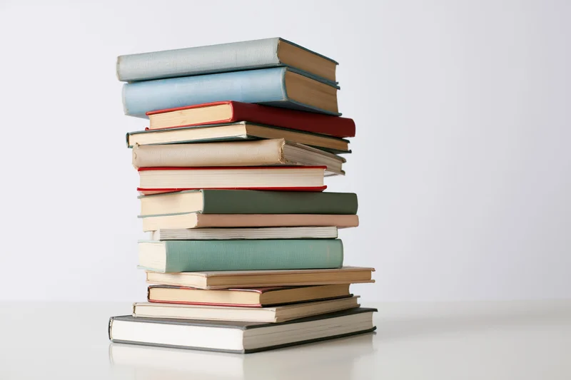 Tall stack of assorted hardcover books arranged vertically on a white surface