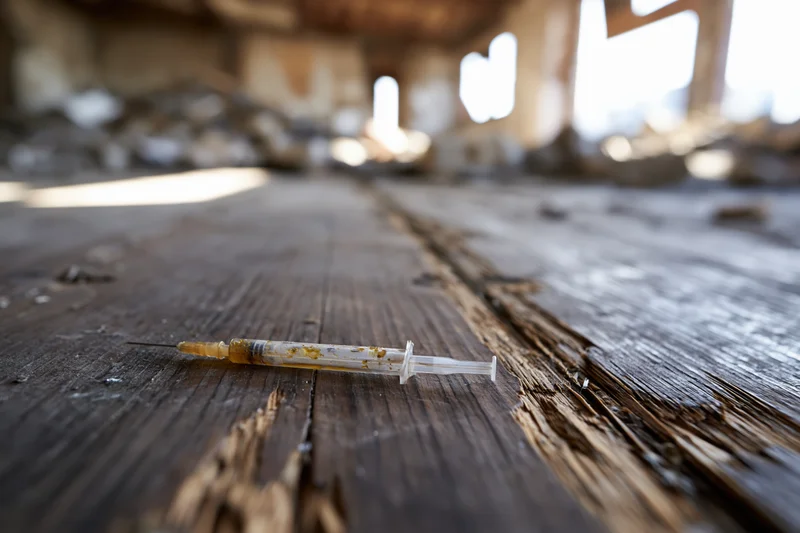 Used syringe with yellow residue lying on a weathered wooden floor in an abandoned building