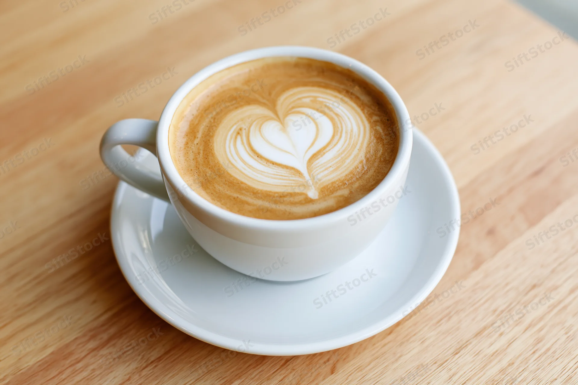 White ceramic cup of latte with heart-shaped foam art on wooden table