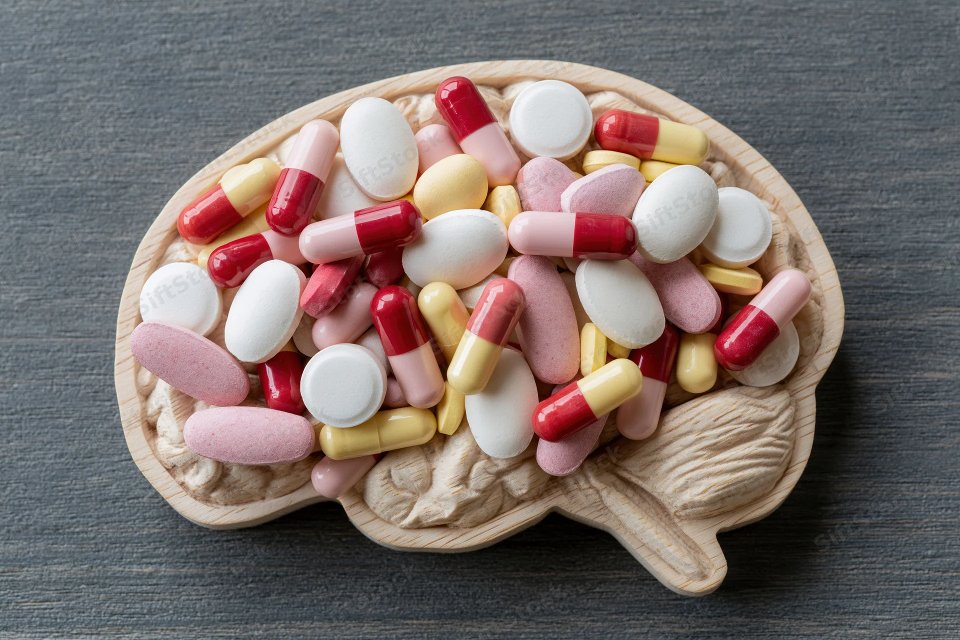 Wooden brain-shaped tray filled with assorted pills and capsules on dark surface