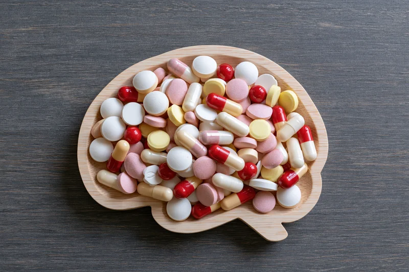 Wooden brain-shaped tray filled with assorted pills on dark surface