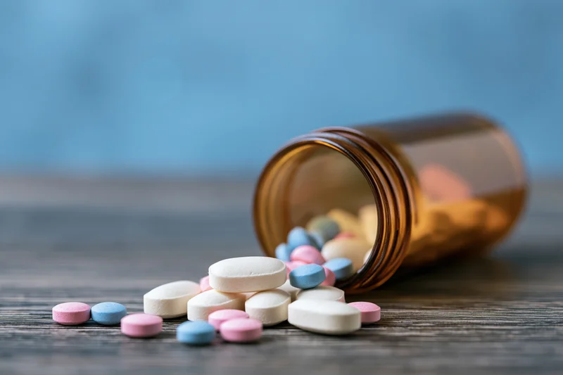 Scattered colorful pills spilling from an amber prescription bottle on a dark wooden surface