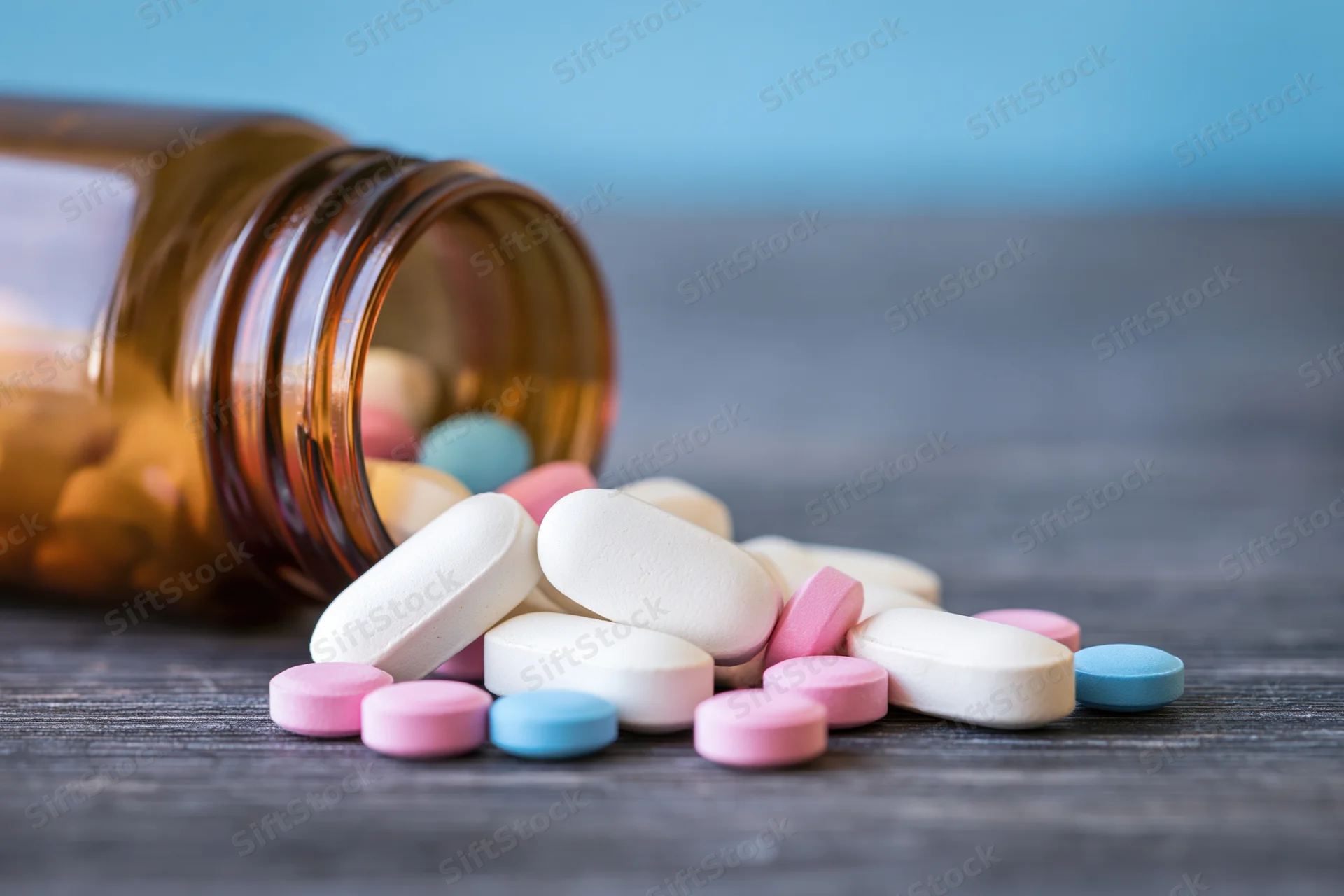 Scattered pills and an amber bottle on a dark wooden surface