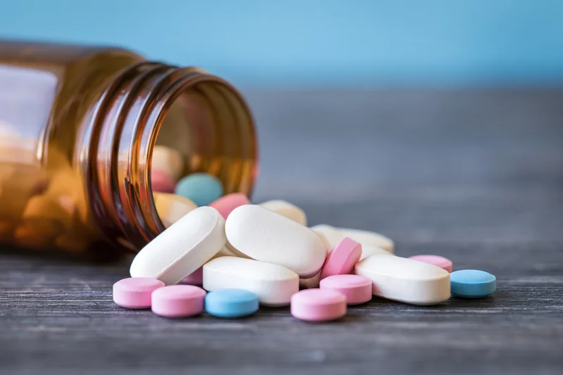 Scattered pills and an amber bottle on a dark wooden surface