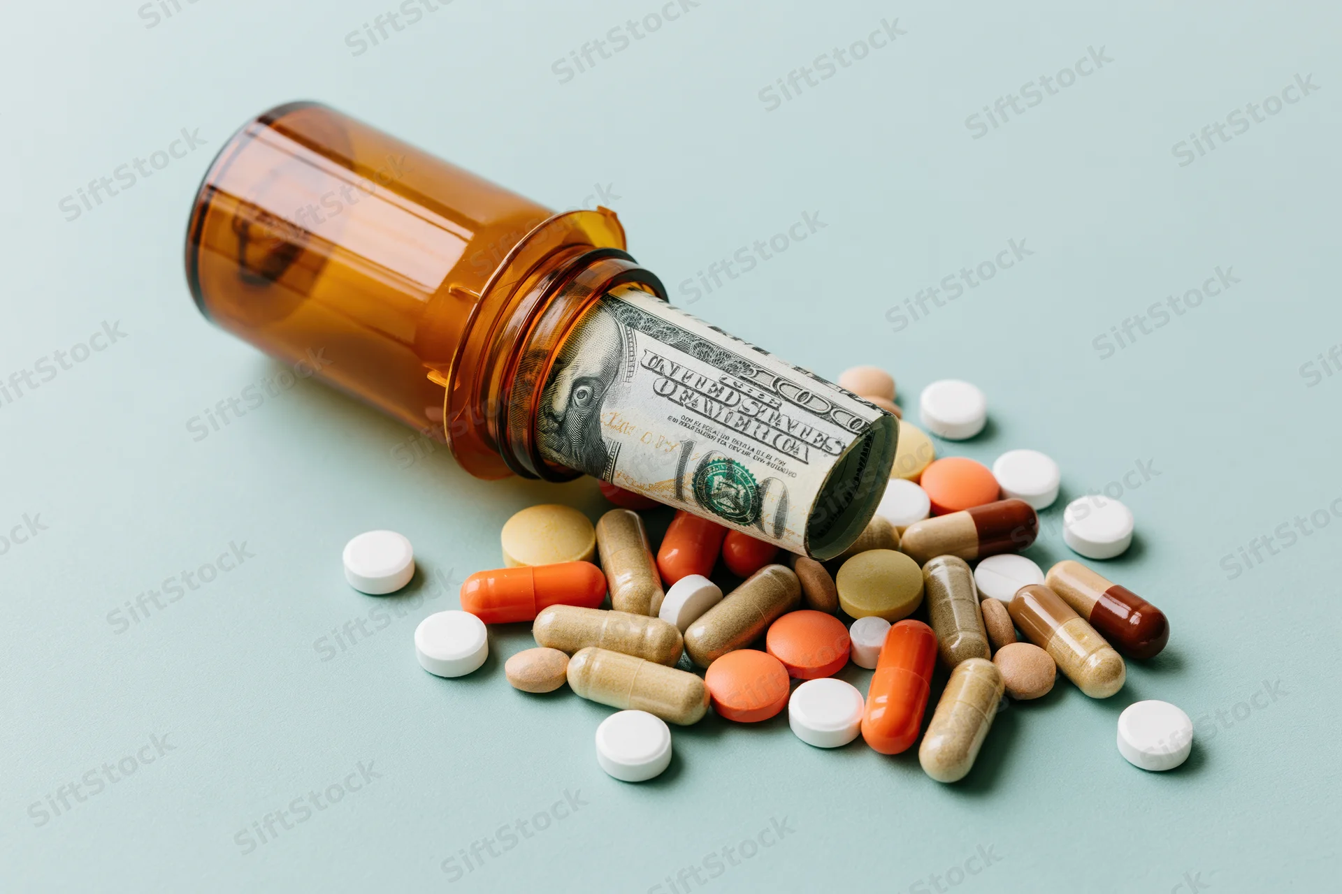 Amber prescription bottle tipped over with pills and a rolled hundred-dollar bill spilling out onto a light blue surface