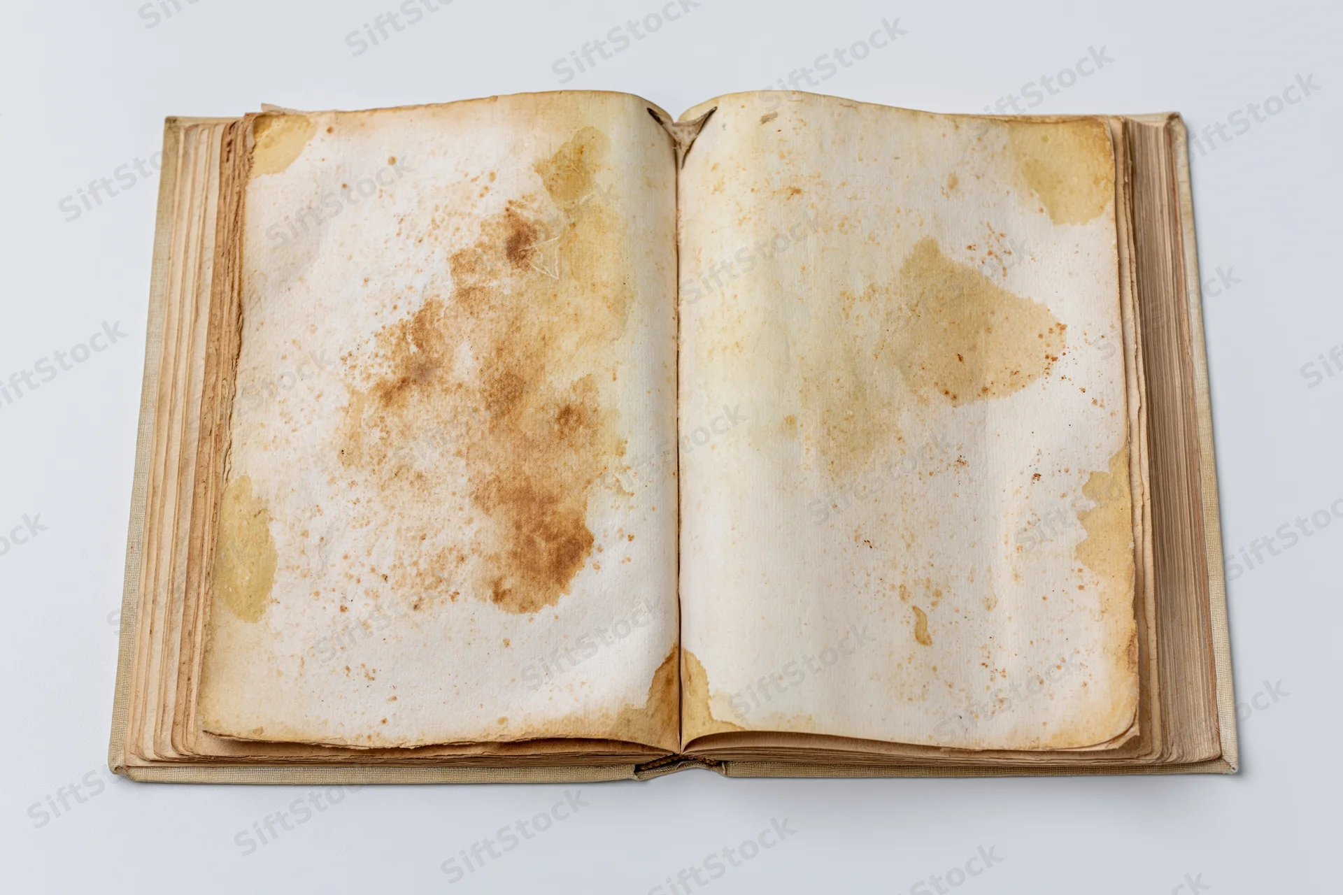 Open vintage book with yellowed stained pages lying flat on white surface
